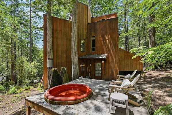 Eine Holzhütte mit Whirlpool, Liegestühlen und Wald im Hintergrund.