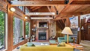 A cozy cabin interior with a fireplace, wooden beams, a sofa, and a television. - Moonraker House | Redwoods, Hot Tub & Trails (Sea Ranch)