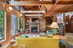 Ein gemütliches Blockhaus-Interieur mit Kamin, Holzbalken, einer Couch und einem Fernseher.