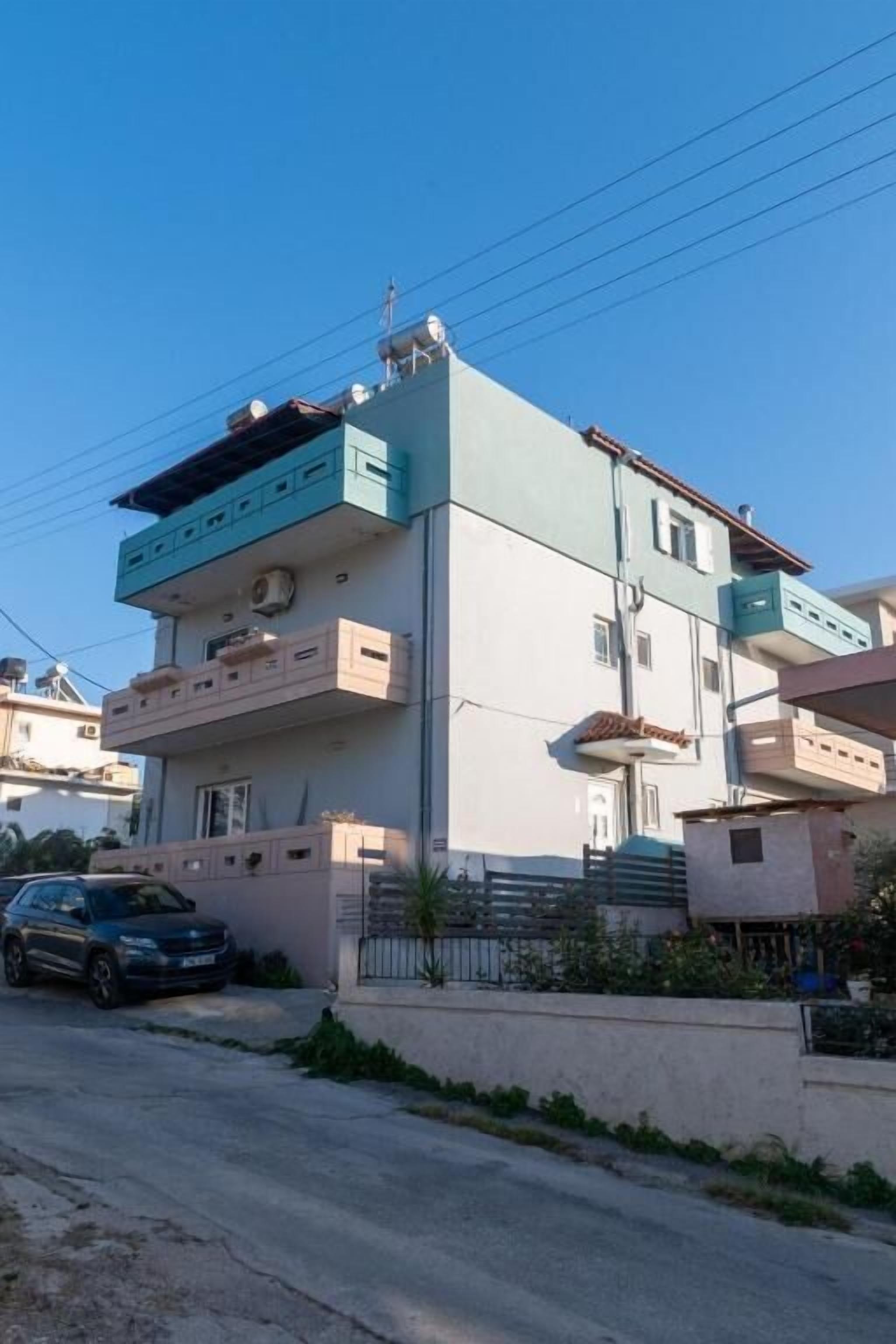 A multi-story residential building with a flat roof, a car parked in front, and a clear sky.