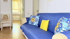 Ein blaues Sofa mit gemusterten Kissen, ein weißer Sessel mit Kissen sowie eine Tür zu einem Badezimmer.