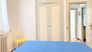 Ein Schlafzimmer mit Bett, Stuhl, Kleiderschrank und einer geöffneten Tür zu einem anderen Raum.