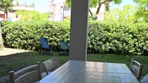 Eine Terrasse mit Tisch und Stühlen, umgeben von einer Hecke und Gebäuden im Hintergrund.