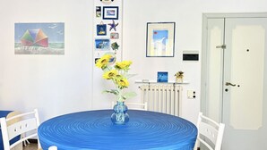 Ein Zimmer mit einem runden Tisch, weißen Stühlen, einer Vase mit gelben Blumen und einer Tür.