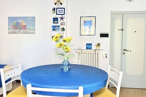 A room with a round table, white chairs, a vase with yellow flowers, and a door. - M436 - Marcelli, three-room apartment with garden, 150 meters from the sea (Marcelli)