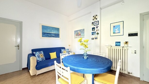 Ein Zimmer mit einem blauen Sofa, einem runden Tisch mit gelben Stühlen und verschiedenen Wanddekorationen.