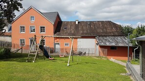 Ein zweistöckiges Haus mit Holzterrasse, Schaukel und umzäunter Garten.