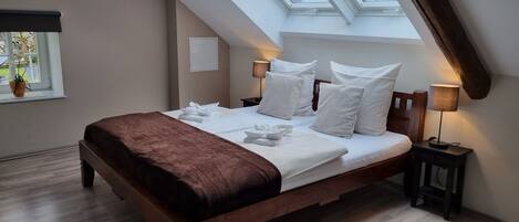 A bedroom with a skylight, a bed with pillows, a bedside table with a lamp, and a window with a plant.