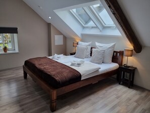 Ein Schlafzimmer mit Oberlicht, einem Bett mit Kissen, einem Nachttisch mit Lampe und einem Fenster mit Pflanze.