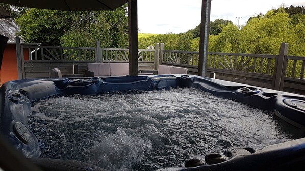 Ein Whirlpool mit Holzterrasse und Geländern, umgeben von viel Grün.