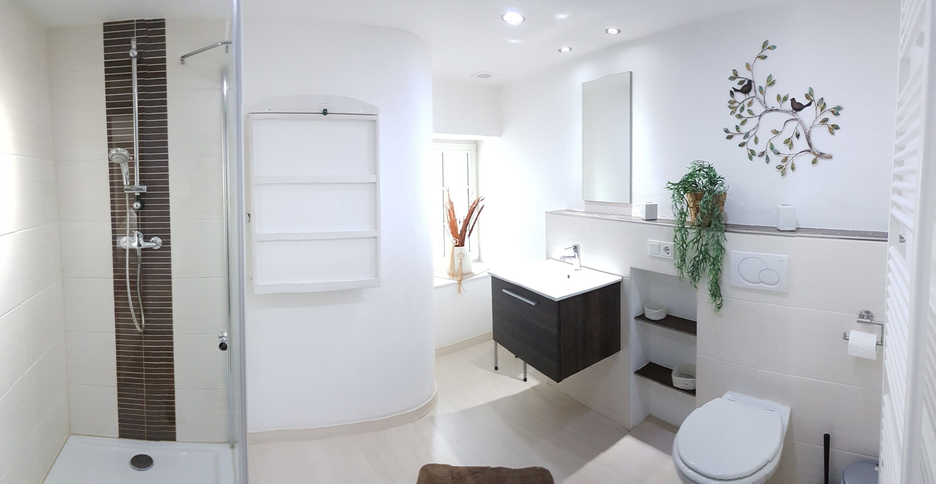 A modern bathroom with a glass-enclosed shower, a white sink, a dark vanity, a toilet, and a decorative wall piece.