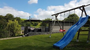 Ein Spielplatz mit einer blauen Rutsche, Schaukeln und einem überdachten Sitzbereich.