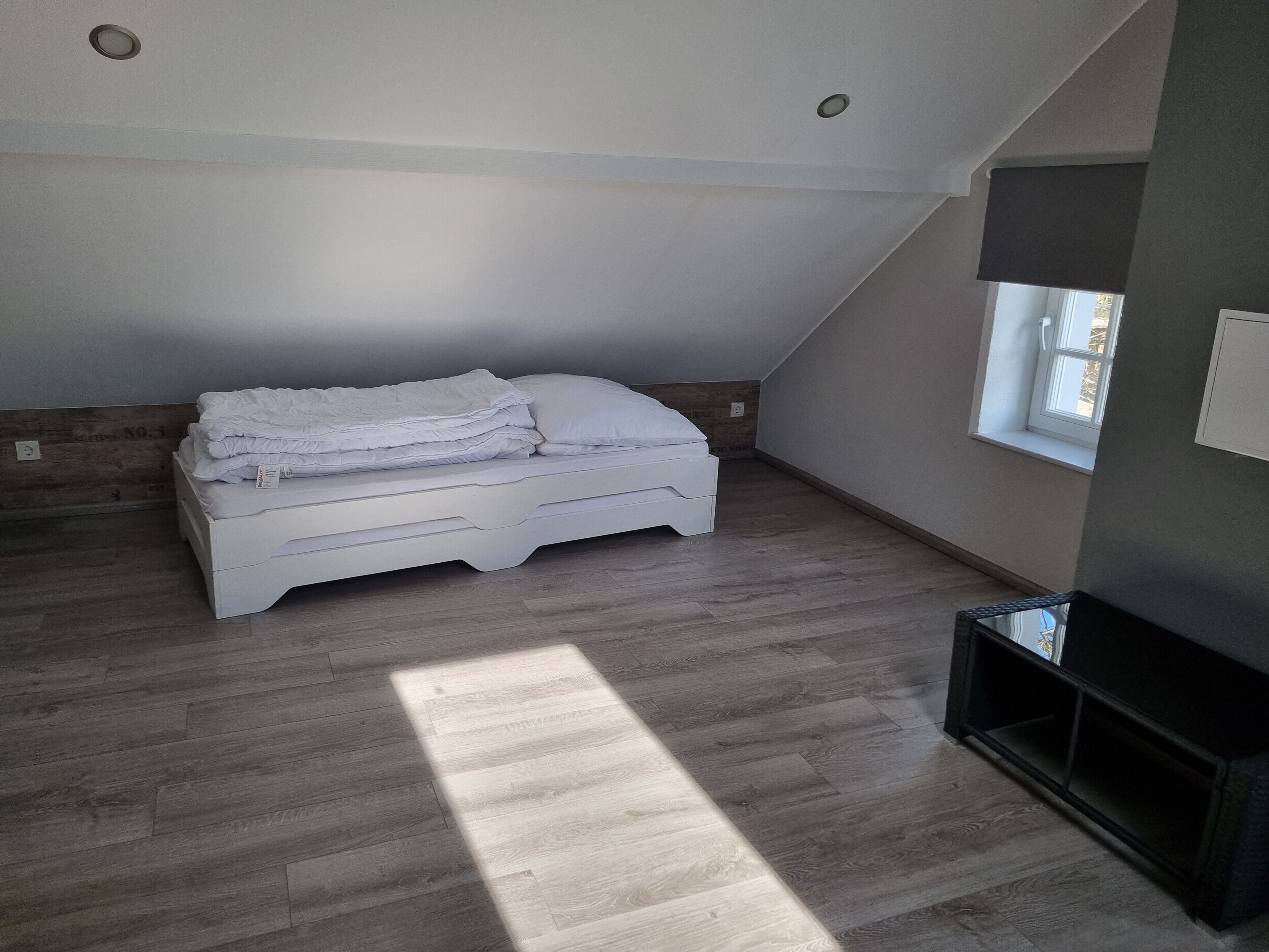A bedroom with a sloped ceiling, a bed, a window, and a built-in TV shelf.
