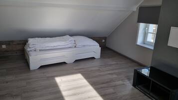 A bedroom with a sloped ceiling, a bed, a window, and a built-in TV shelf.