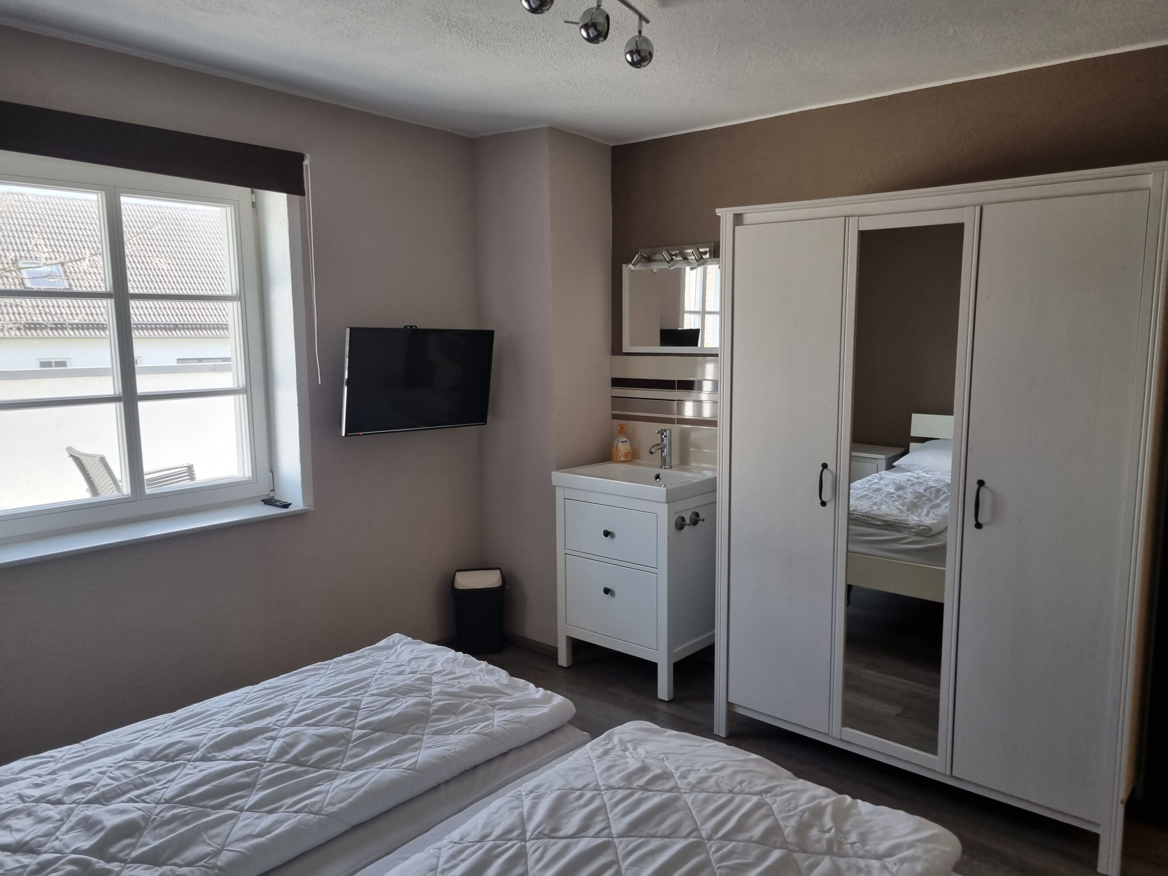 Een slaapkamer met een bed, een kast, een televisie, een raam en een badkamer.
