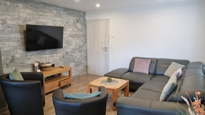 Ett vardagsrum med en platt-TV, en soffa, ett soffbord och ett litet sidobord i trä.