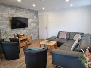 A living room with a flat-screen TV, a sofa, a coffee table, and a wooden side table. - Eifel Dream Schneifelhaus with Private Outdoor Hot Tub and Barrel Sauna (Roth bei Prüm)
