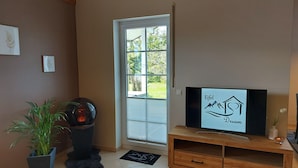 Ein Zimmer mit Fernseher auf einem Holzboden, einer Topfpflanze und einer Tür, die nach draußen führt.
