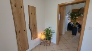 Ein Flur mit Wandkunst aus Holz, einem Blumentopf und einer Tür zu einem Wohnbereich mit einer Couch und einer Pflanze.