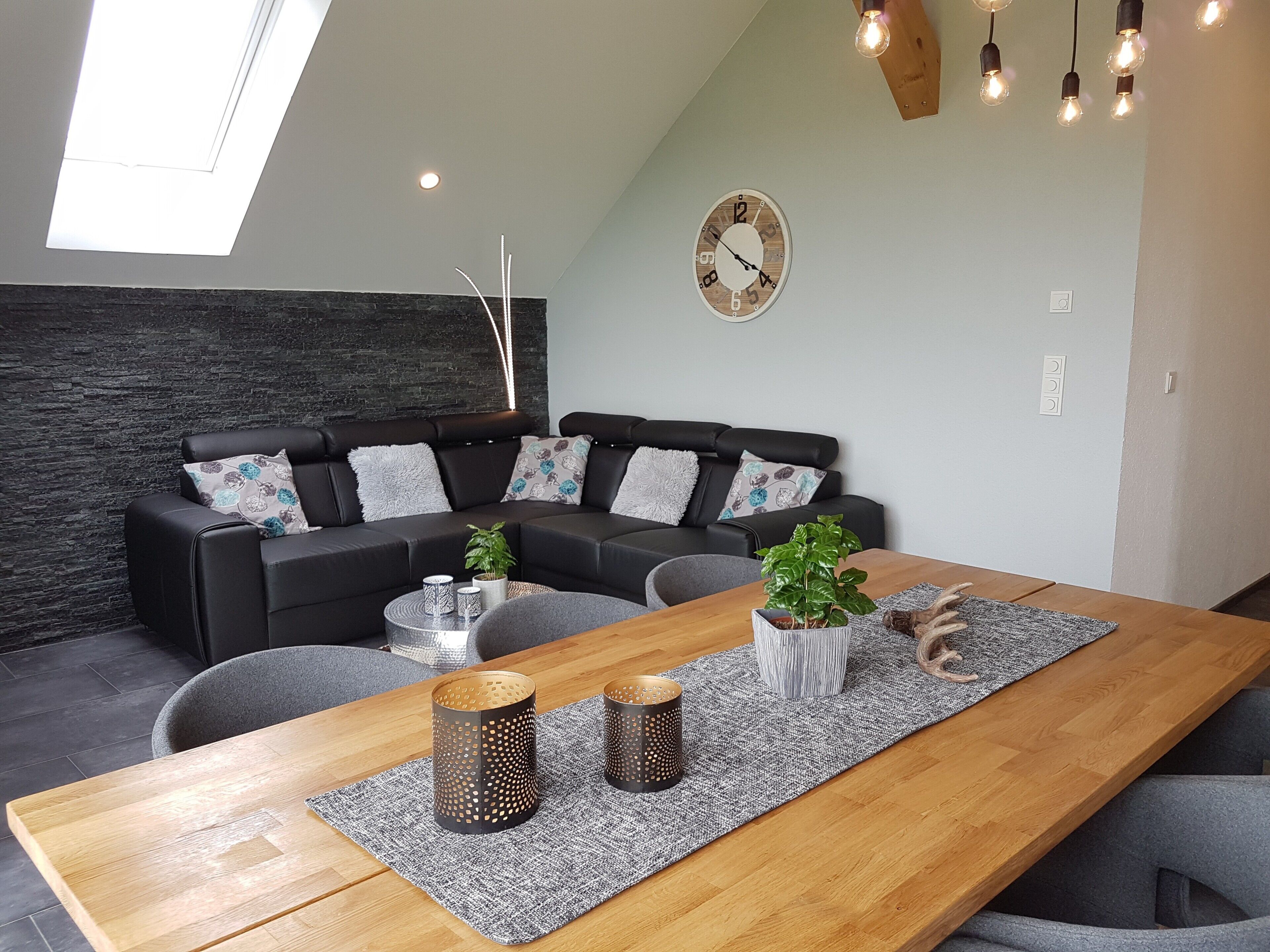 Een moderne woonkamer met een zwarte hoekbank, een houten eettafel en een wandklok.