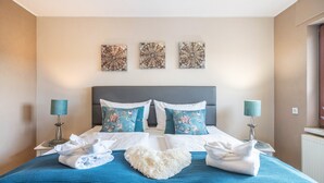 Une chambre d’hôtel avec un lit, deux lampes, un coussin en forme de cœur et trois œuvres d’art murales.