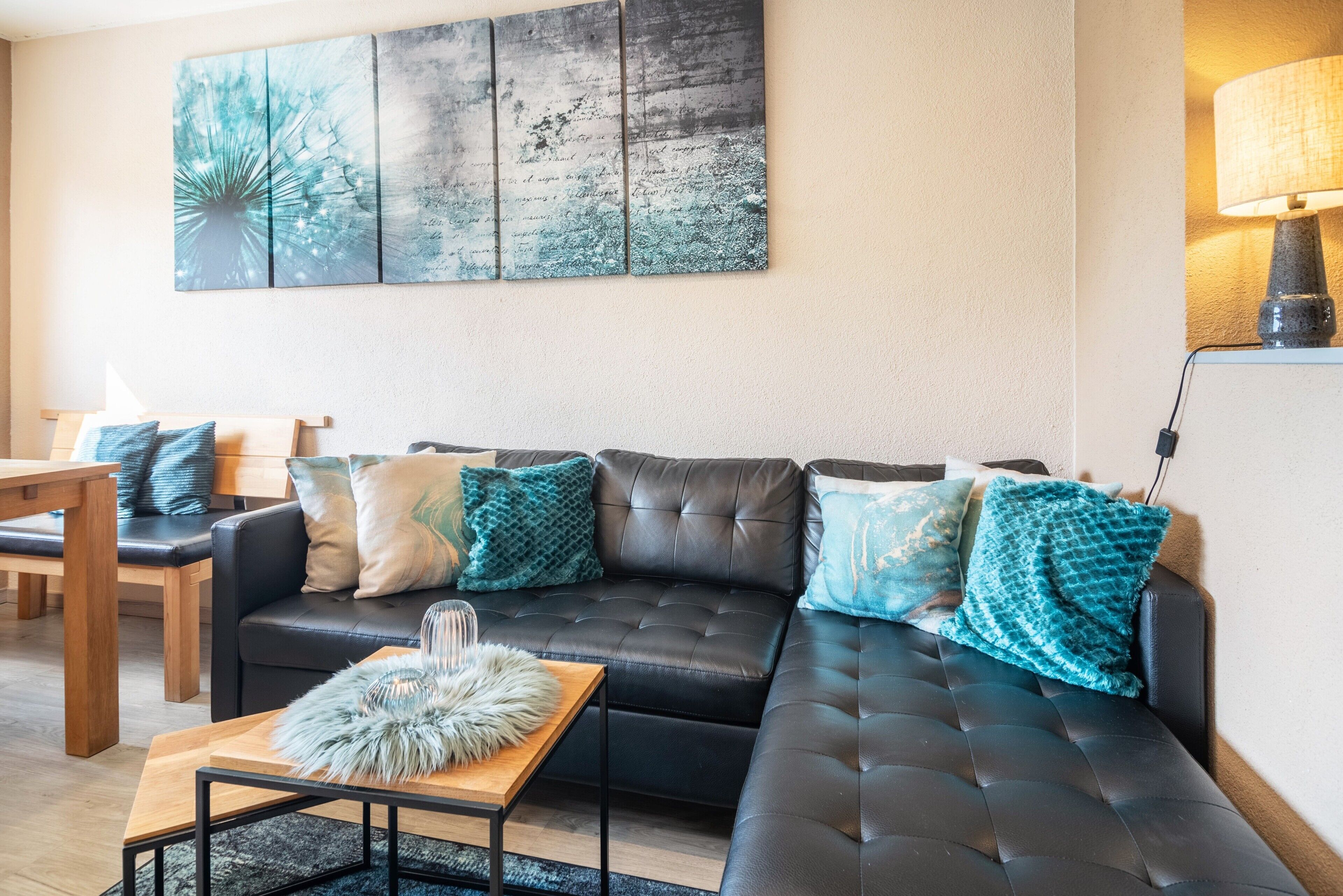 A living room with a black leather sofa, a wooden coffee table, and teal cushions.