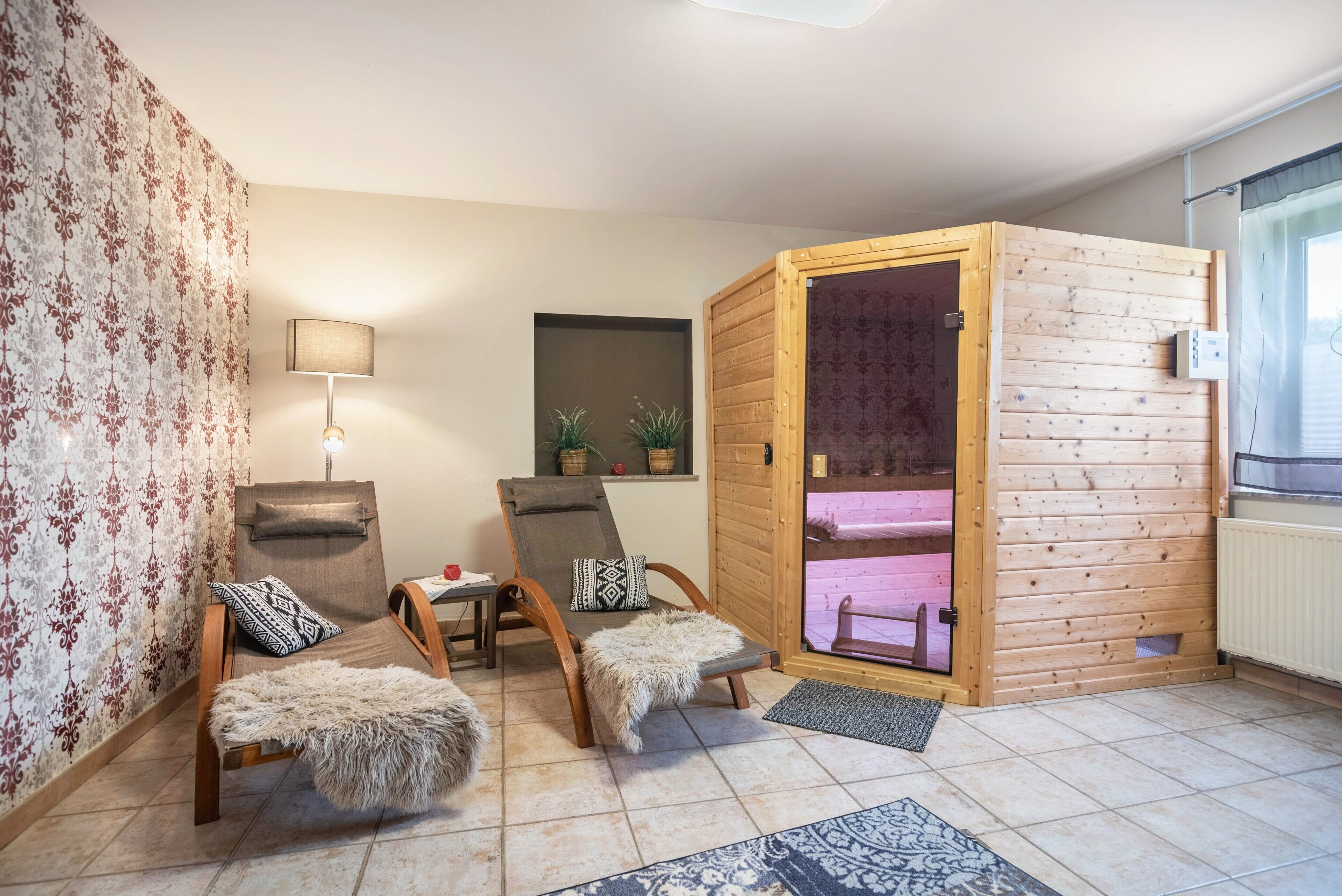 A cozy room with a wooden sauna, two chairs with fur throws, a lamp, and a window with curtains.