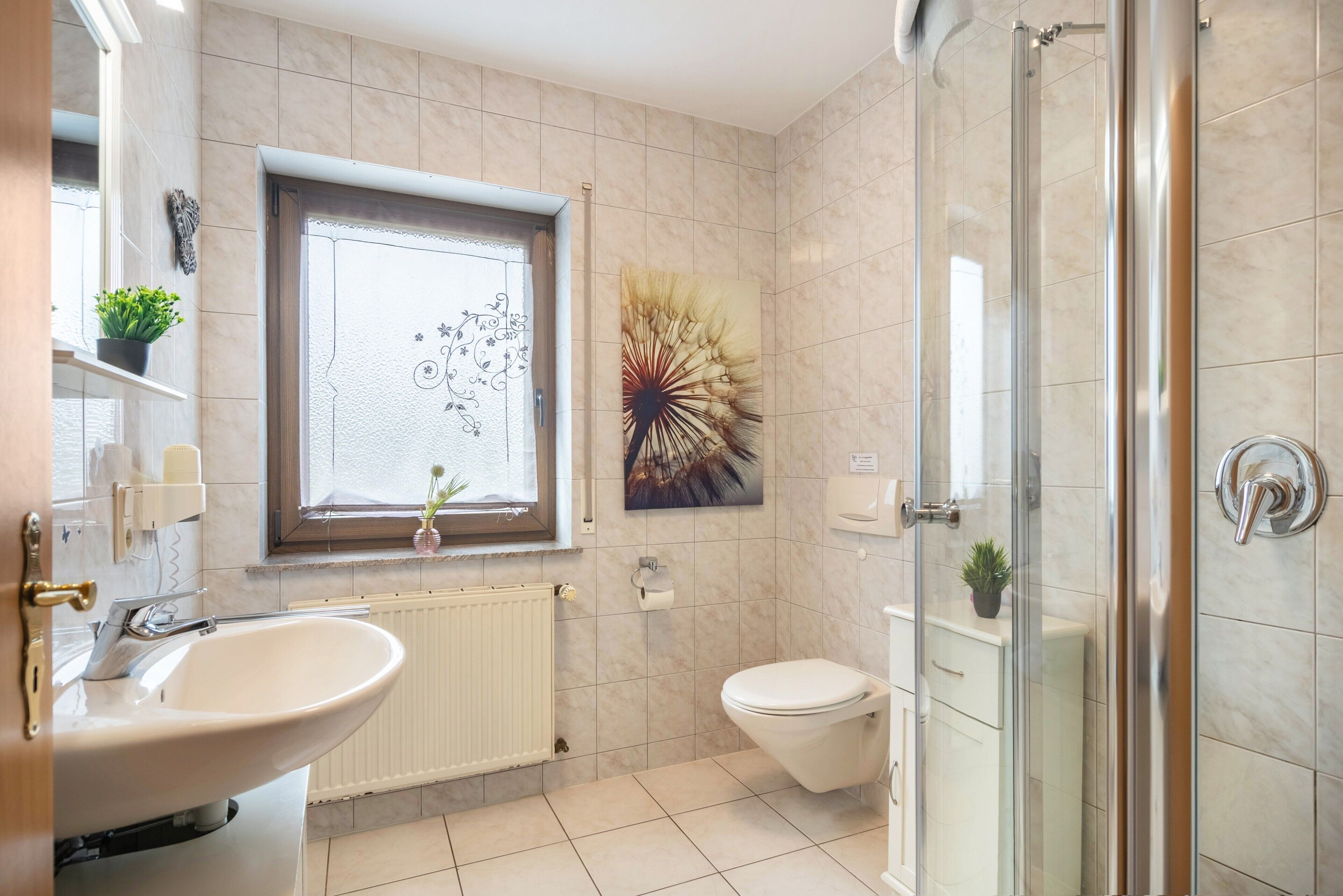 A bathroom with a sink, toilet, shower, and a window with a decorative view.