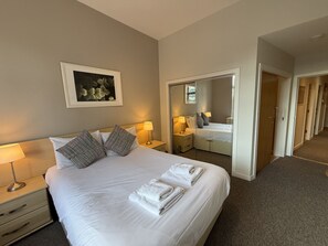 Ein Hotelzimmer mit Bett, Nachttischen, einem Spiegel und einer Tür zu einem Flur.