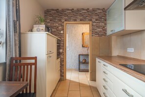 A compact kitchen with a stone backsplash, a wooden chair, and a white cabinet.