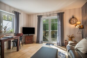 A living room with a flat-screen TV, a wooden cabinet, a leather sofa, and a dining area with a table and chairs.