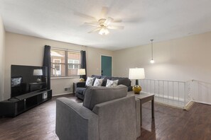 Ein Wohnzimmer mit Flachbildfernseher, grauem Sofa und Deckenventilator.