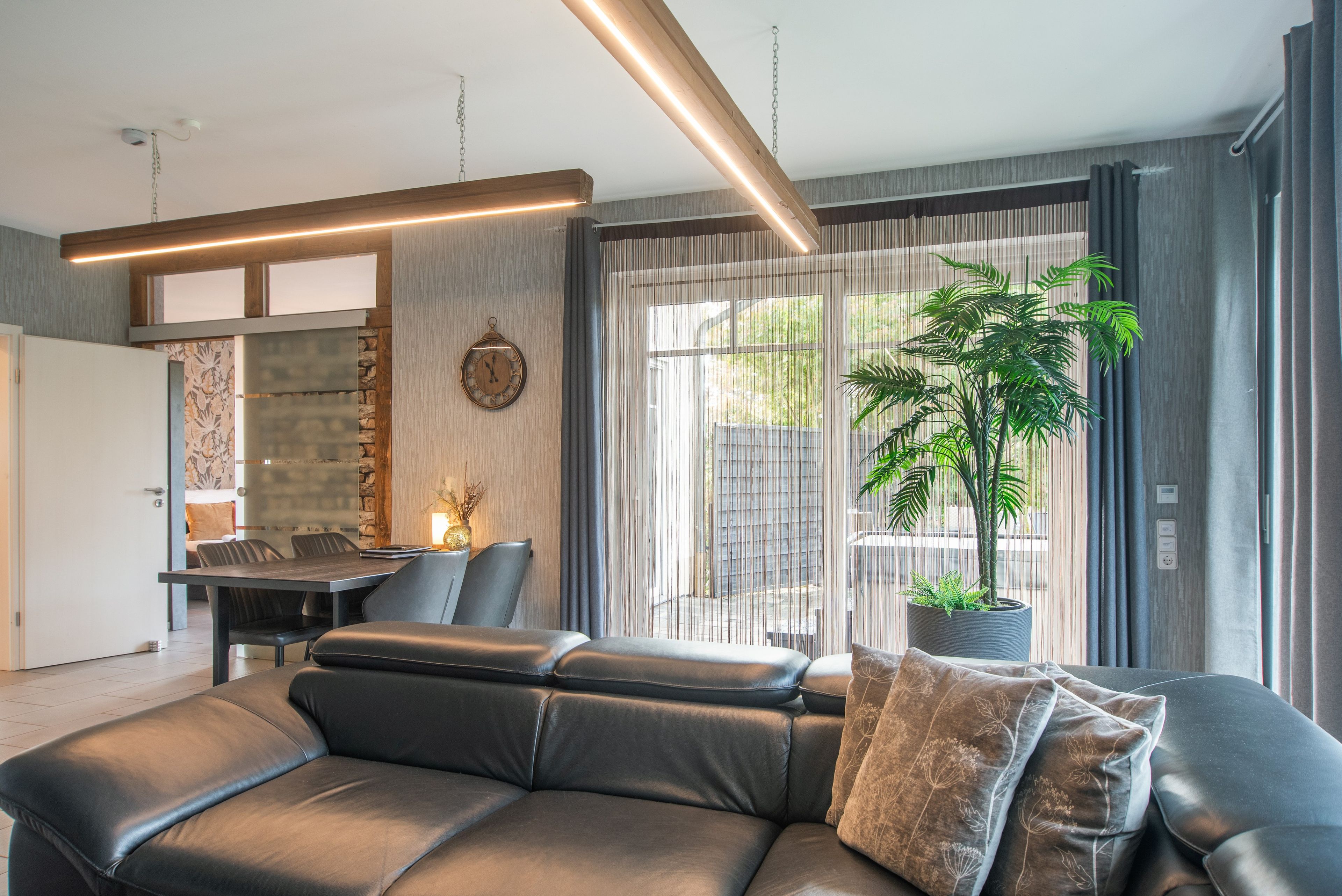 A modern living room with a leather sofa, a dining area, and a large window with curtains.