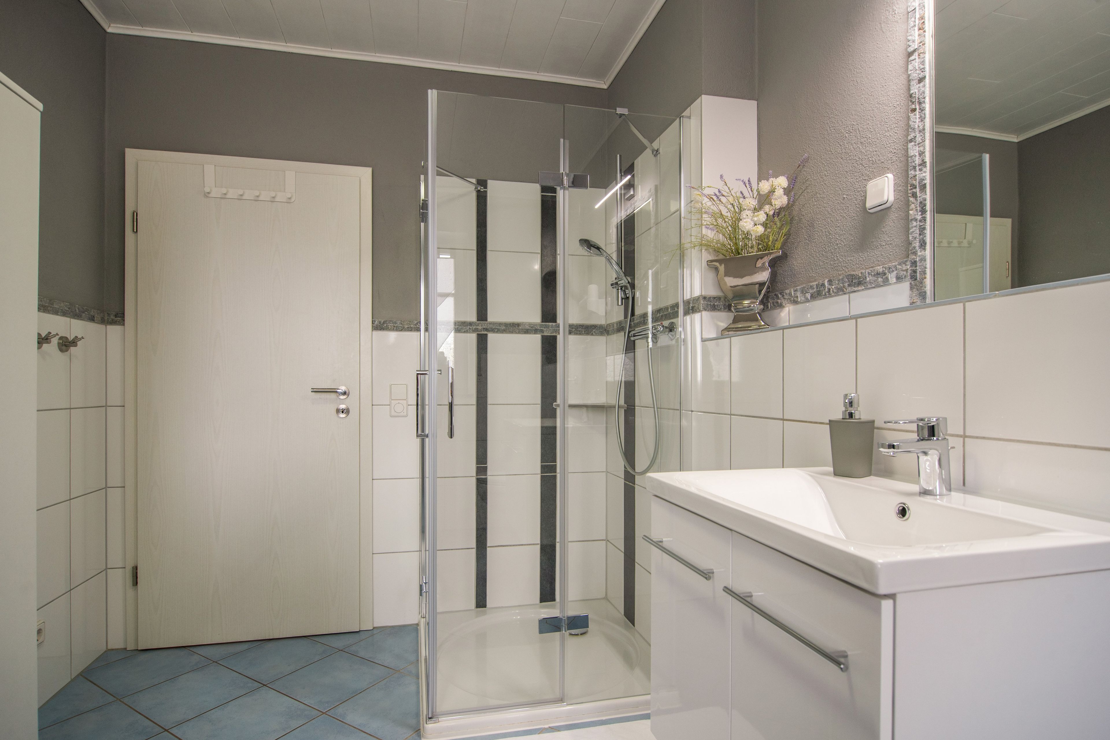 A bathroom with a glass shower enclosure, a white sink, and a mirror above the sink.