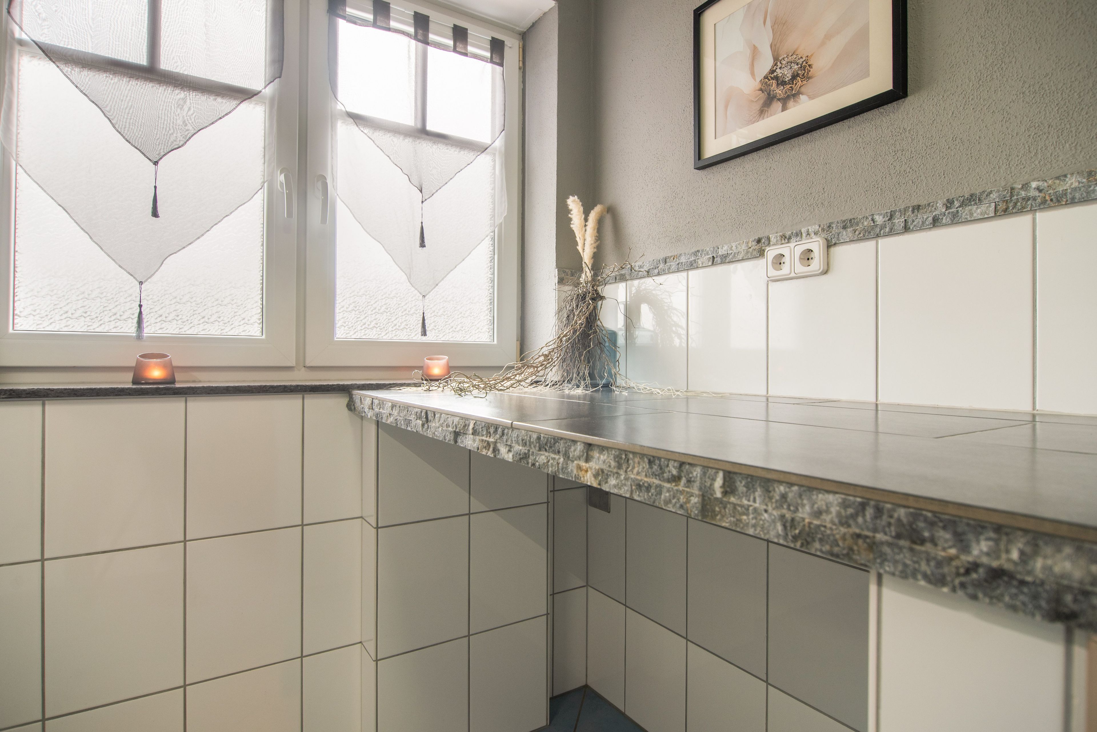 Cocina con paredes de azulejos blancos, encimera de granito y ventana con celosía decorativa.