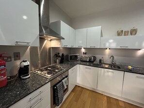 A modern kitchen with white cabinets, a stainless steel range hood, a gas stove, a microwave, and a toaster. - Ingram One Bedroom Apartment (Glasgow)
