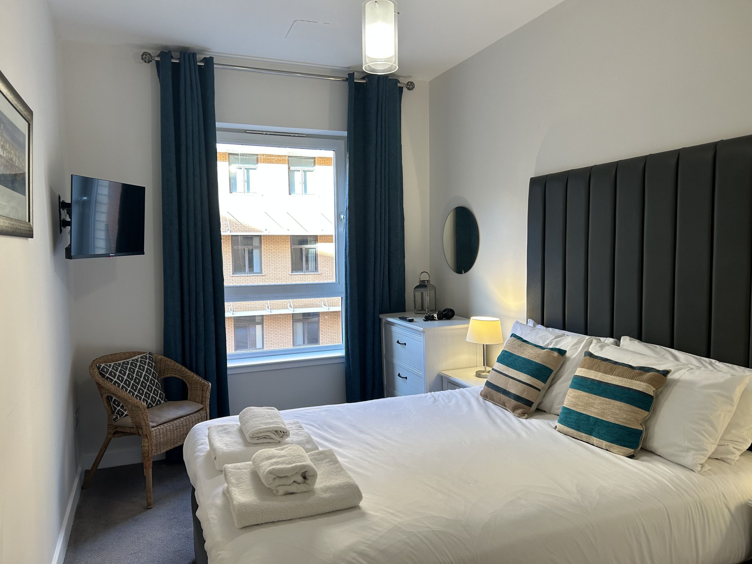 Una habitación de hotel con una cama, una silla, una mesita de noche, una lámpara y un televisor.
