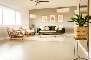 A living room with a green sofa, two wicker chairs, a coffee table, and a ceiling fan. - Cheerful 2-Bedroom JTree House with Hot Tub and Cowboy Pool (Joshua Tree)