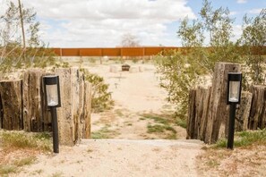 A dirt path leading to a building with a wooden fence and a metal gate. - Cheerful 2-Bedroom JTree House with Hot Tub and Cowboy Pool (Joshua Tree)