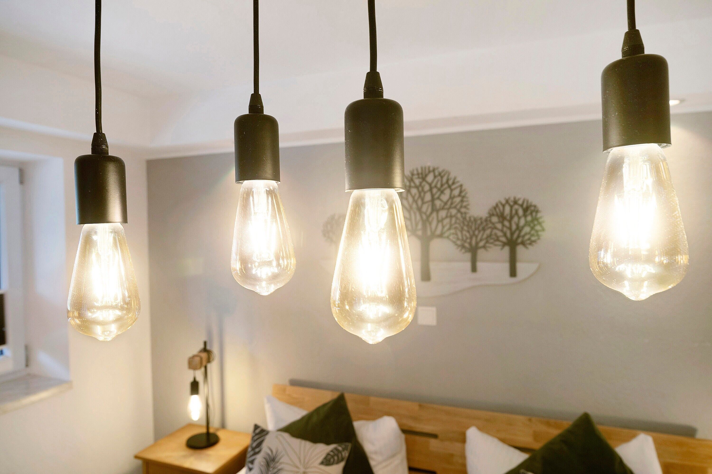 Une chambre avec une tête de lit en bois, une table de chevet avec une lampe et un mur décoré d’un motif d’arbre.
