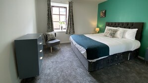 Ein Schlafzimmer mit Bett, Schreibtisch, Stuhl, einem Fenster mit Vorhängen und einer Deckenleuchte.