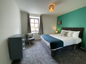 Ein Schlafzimmer mit Bett, Schreibtisch, Stuhl, einem Fenster mit Vorhängen und einer Deckenleuchte.