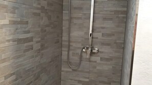 Una ducha con puerta de vidrio, cabezal de ducha de mano y pared con diseño tipo piedra.