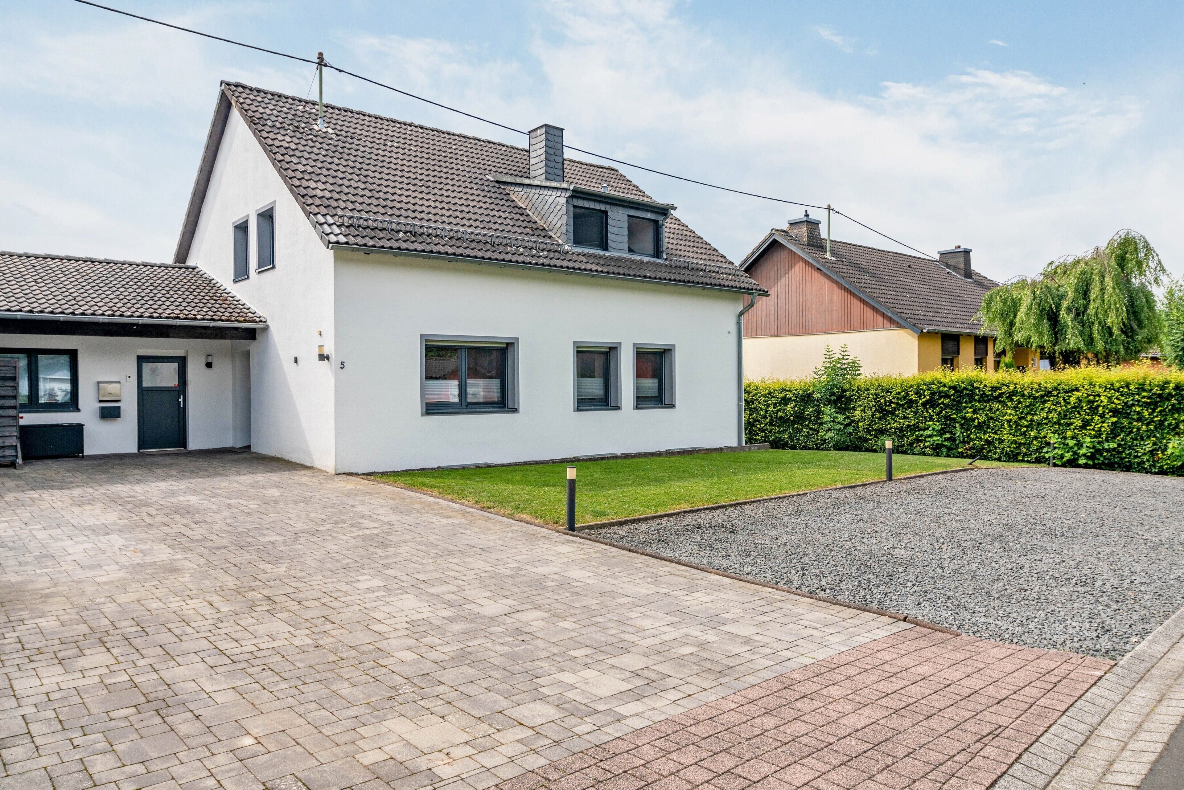 Une maison d’habitation avec une allée pavée, une petite pelouse et une haie.