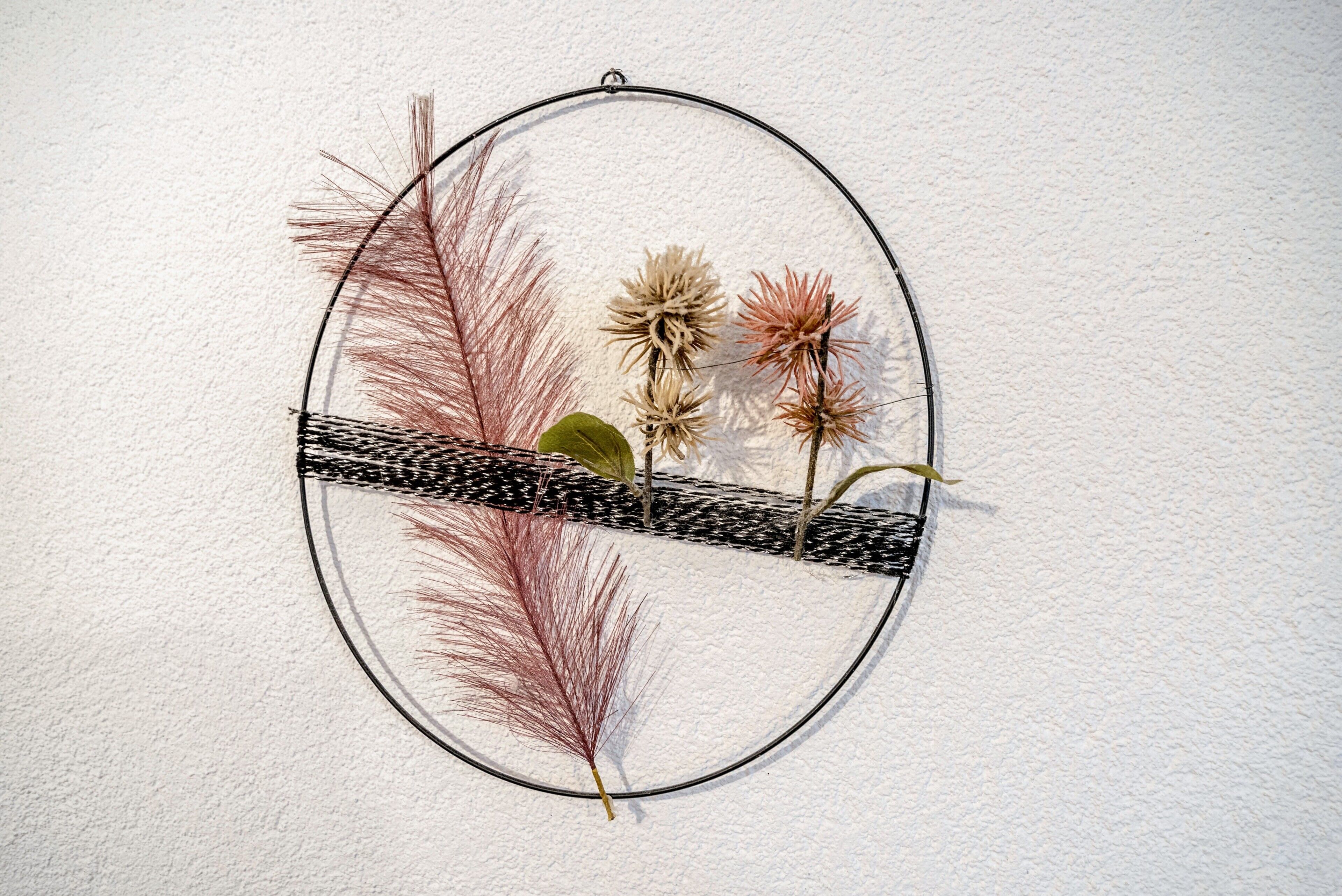Decoración de pared circular con plantas secas y una franja estampada en blanco y negro.