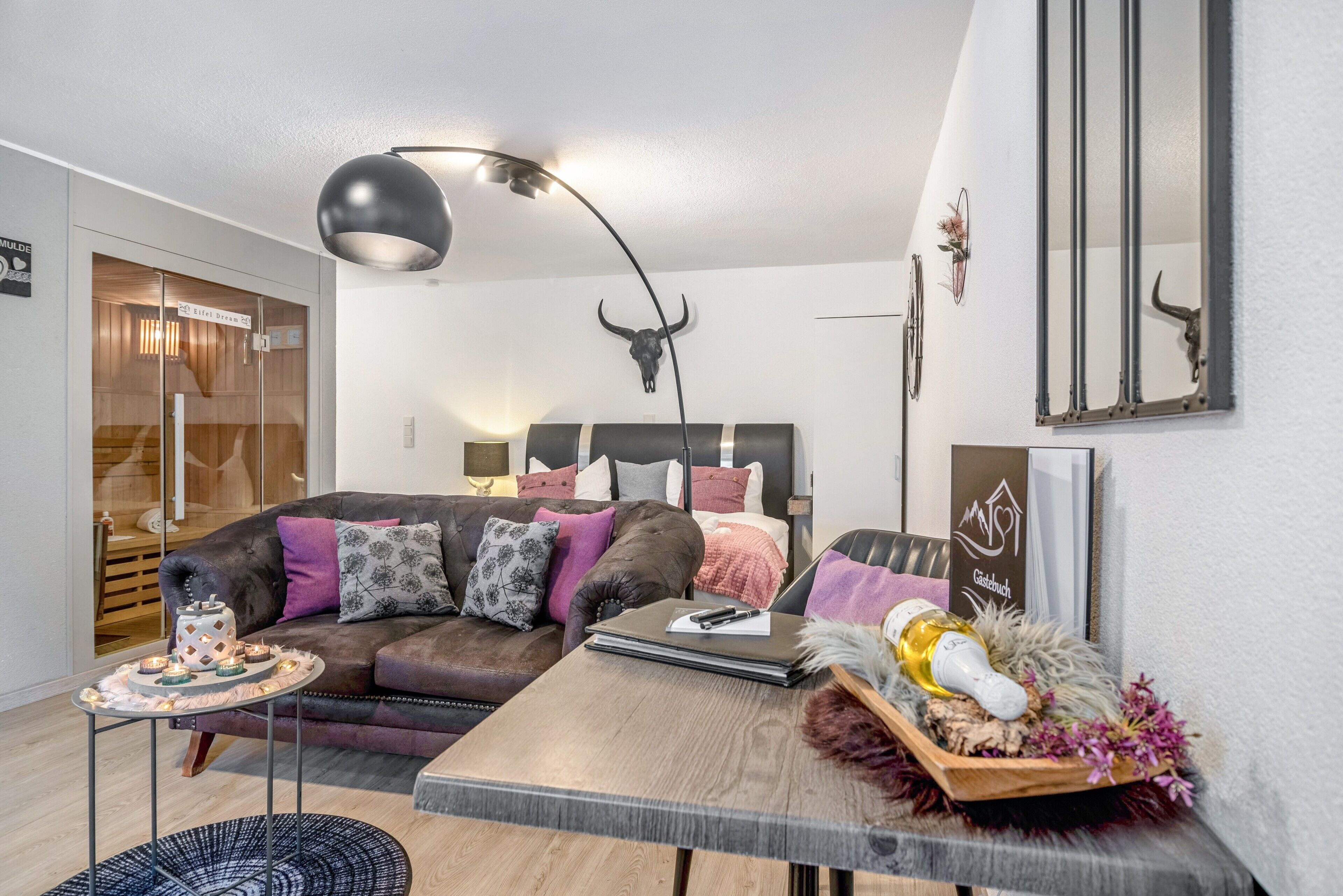 Una sala moderna con un sofá, una mesa con un cuenco decorativo, una lámpara y un espejo montado en la pared.