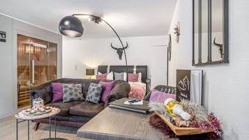 Una sala moderna con un sofá, una mesa con un cuenco decorativo, una lámpara y un espejo montado en la pared.