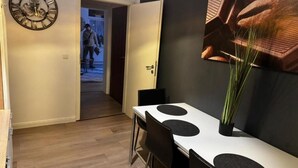 Un comedor con una mesa blanca y sillas negras, un reloj de pared grande y un acceso a otra habitación.