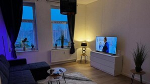 Una sala de estar con sofá, mesa de centro, televisión y lámpara.
