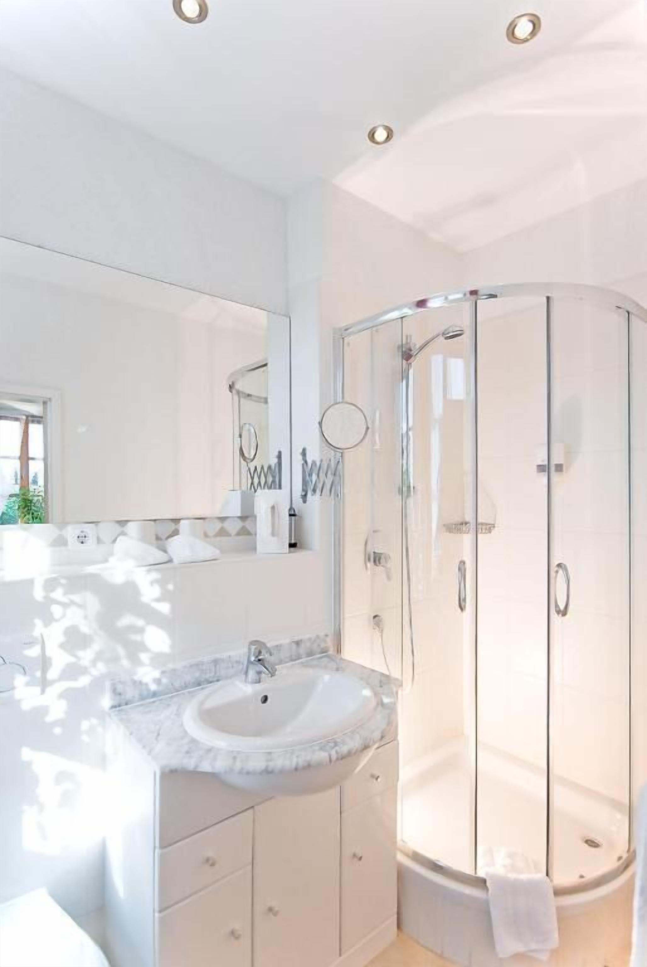 Een moderne badkamer met een douche in een glazen cabine, een wastafel met een marmeren blad en een grote spiegel.